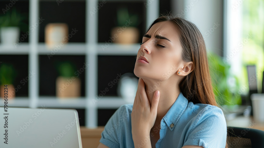 a girl sits at an office desk and suffers from neck pain, touches her stiff neck with her hand , copy space