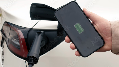 A man checks a phone app to charge his electric car at a charging station, close-up.