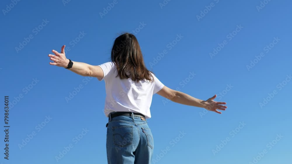 A free and happy young woman is spinning against the background of a serene blue sky on a sunny summer day. A free and happy young woman is spinning against the background of a serene blue sky on a sunny summer day.