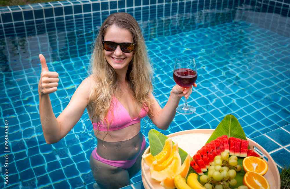 Beautiful woman in the swimming pool with glass of wine and floating tray of fruits Beautiful woman in the swimming pool with glass of wine and floating tray of fruits