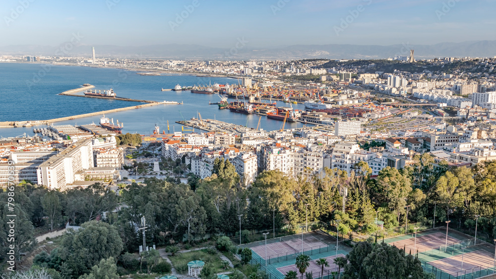 Algiers sea bay and pier port, aerial view on the capital city buildings, tennis court, trees and Mediterranean blue water ships and boats. The Great mosque and the Martyr's Memorial monument.