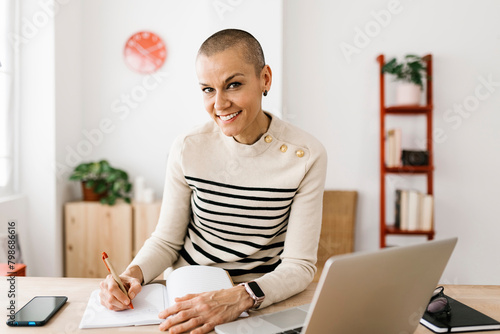 Portrait of mid adult businesswoman smiling at camera working with laptop at home office. Business and technology lifestyle concept.