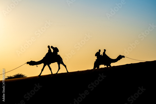 Silhouette of camel with two people sitting on it crossing over sand dunes in Sam Jaisalmer Rajasthan India