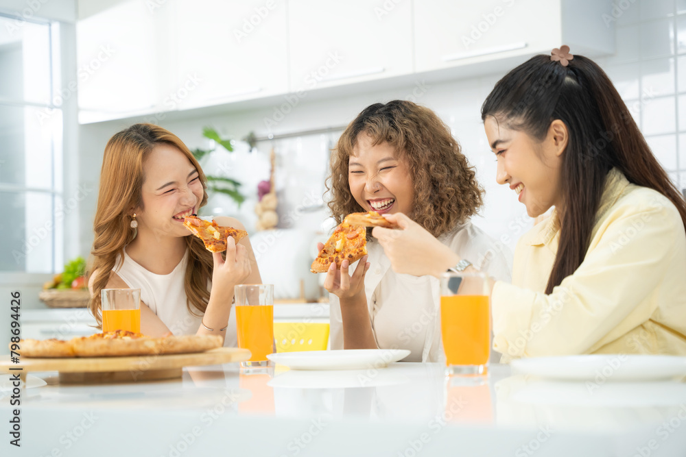 Three friends enjoying a delicious pizza meal together, laughing and drinking orange juice in a sunlit kitchen. Three friends enjoying a delicious pizza meal together, laughing and drinking orange juice in a sunlit kitchen.