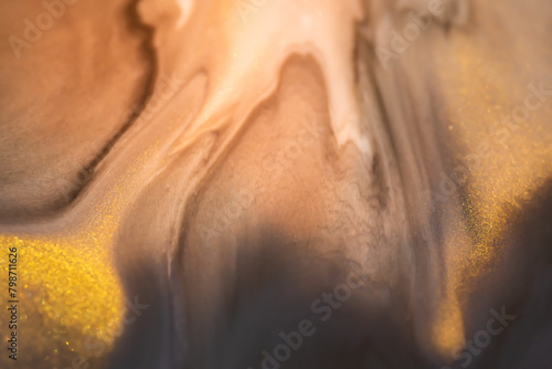 Beige and brown acrylic paints with shimmering golden glitter. Liquid paint abstract background.