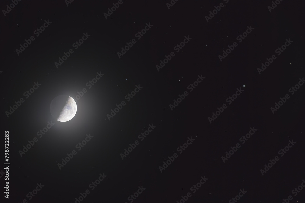 Naklejka premium The mineral Moon in its first quarter phase, in conjunction with the star Pollux in the Gemini constellation and some background stars. You can see the earth-shine in the shadowed part.