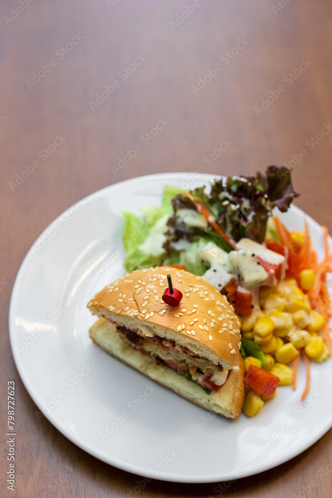 hamburger white sesame or chicken burger cut in half with vegetable and fruits salad by ripe papaya sweetcorn watermelon lettuce and dragon fruit for diet food in plate on wooden table with copy space