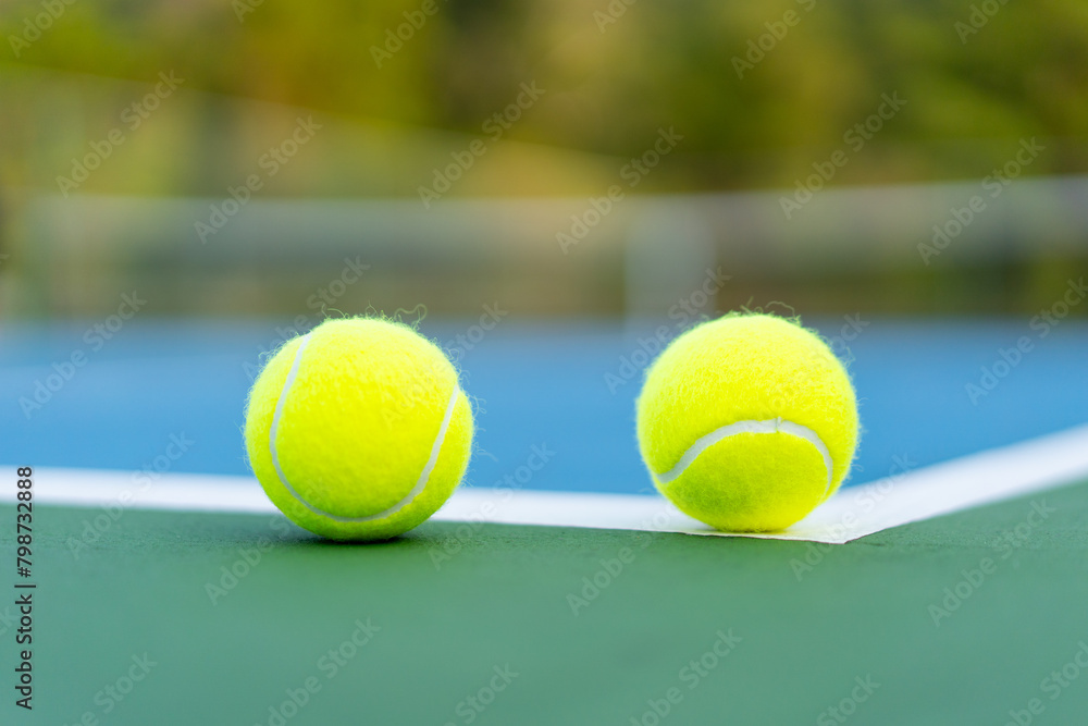 tennis balls on white line of green and blue hard court with blurred court as background