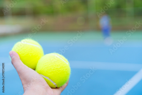 two tennis balls in left hand, selective focus, blurred player and blue tennis court as background