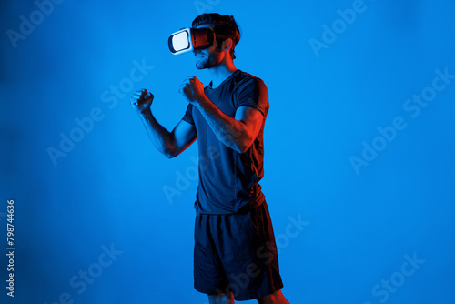 Happy man with VR goggle exercising and stretching arm at neon light background. Caucasian person with casual cloth relaxing and exercising by using virtual reality simulator technology. Deviation. © Summit Art Creations