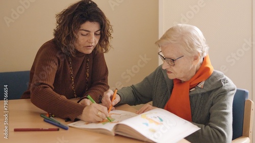 Caregiver and senior woman coloring a draw in a geriatric