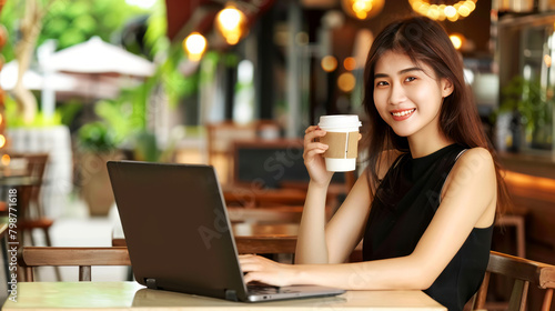 Smiling young Asian woman working on laptop in cafe with a coffee cup  digital nomad lifestyle