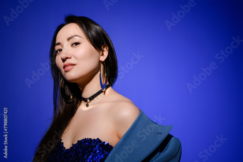 Portrait of confident and stylish asian woman in dress and choker isolated on blue 