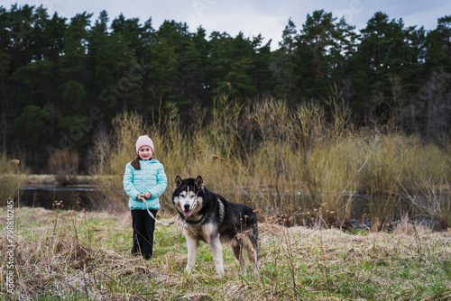 A little girl walks with a husky dog ​​in nature in the forest near Pirita river in the spring.