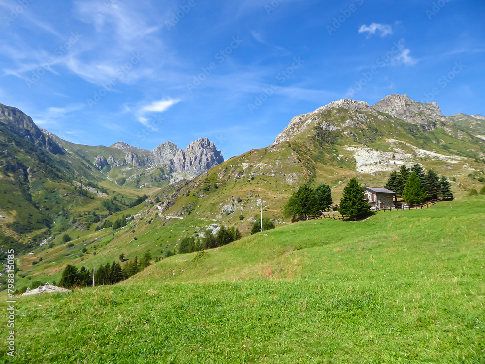 Panoramic mountain landscape of Cottian Alps in Grana Valley (Valle Grana) with clear blue sky on a sunny summer day, Castelmagno, Cuneo, Piedmont, Italy. Wodden cottage on alpine pasture