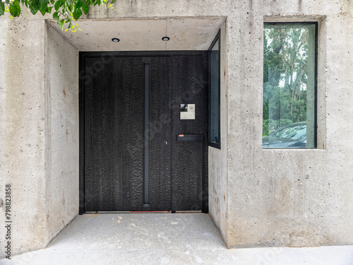 A modern design house entrance with a metal door between rough cement walls and a surveillance window in the upscale suburbs of Athens. Travel to Greece.