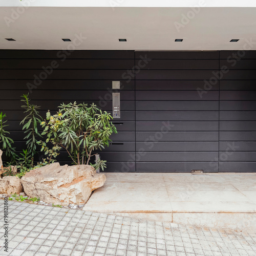 A modern design house entrance with a dark metallic door and a decorative plants in the upscale suburbs of Athens. Travel to Greece.