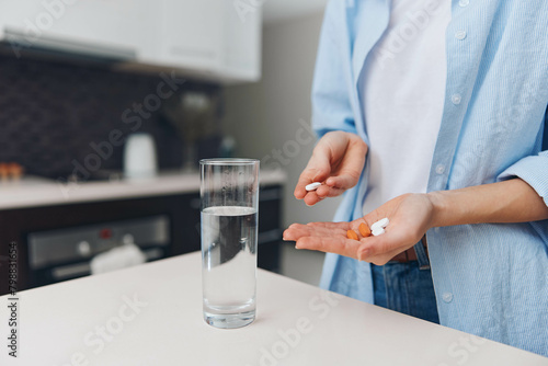Woman taking medication with a glass of water and pill bottle on kitchen counter  healthcare concept