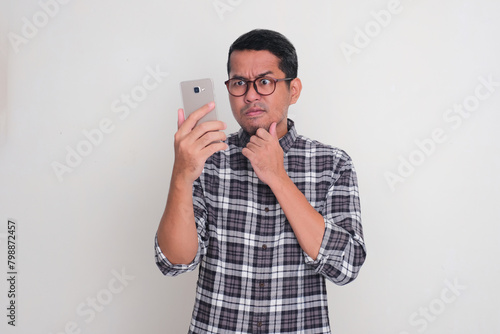 A man looking to his mobile phone with suspicious face expression