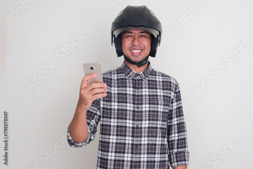 A man wearing motorcycle helmet smiling at the camera while holding mobile phone