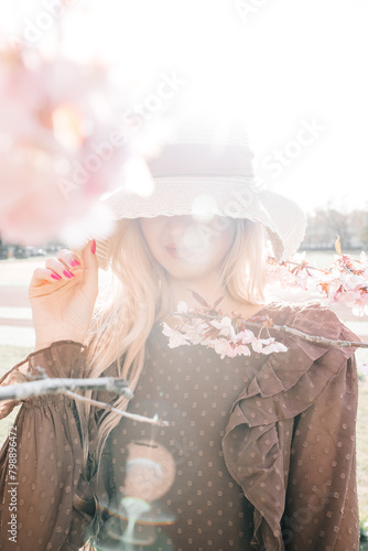 Young pretty woman in hat standing in blooming sakura tree
