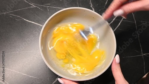Close-up of a woman's hand whisking eggs in a transparent glass bowl. beating egg process.