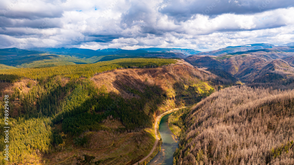 Fototapeta premium Spectacular view of mountains and river in the wilderness of Oregon State, the USA. Mt. Hood National Forest. Grey rainy clouds overcast the sky above the landscape. Top perspective.