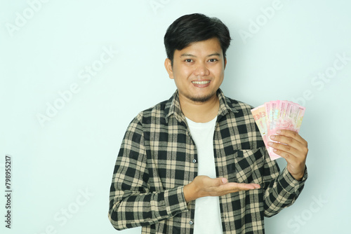 Young Asian man wearing brown flannel shirt smiling happy while holding money with his open right hand photo
