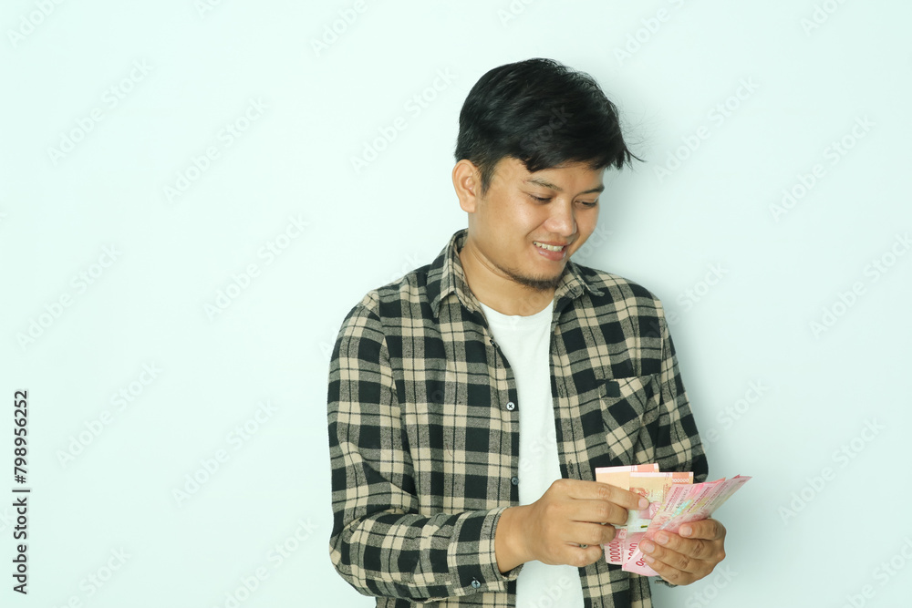 Young Asian man wearing brown flannel shirt smiling happy when counting money that he hold Young Asian man wearing brown flannel shirt smiling happy when counting money that he hold