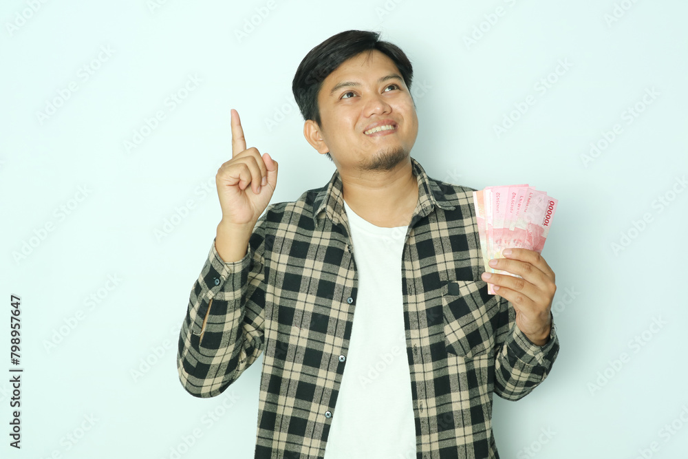 Young Asian man smiling happy and pointing finger up while holding paper money Young Asian man smiling happy and pointing finger up while holding paper money