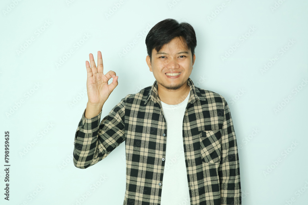 Young Asian man smiling friendly while giving the right finger sign OK Young Asian man smiling friendly while giving the right finger sign OK