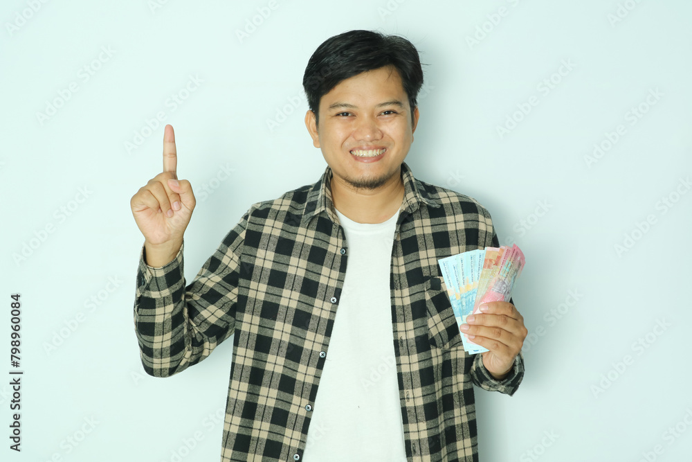 Young Asian man holding paper money while pointing his right finger up and smiling Young Asian man holding paper money while pointing his right finger up and smiling
