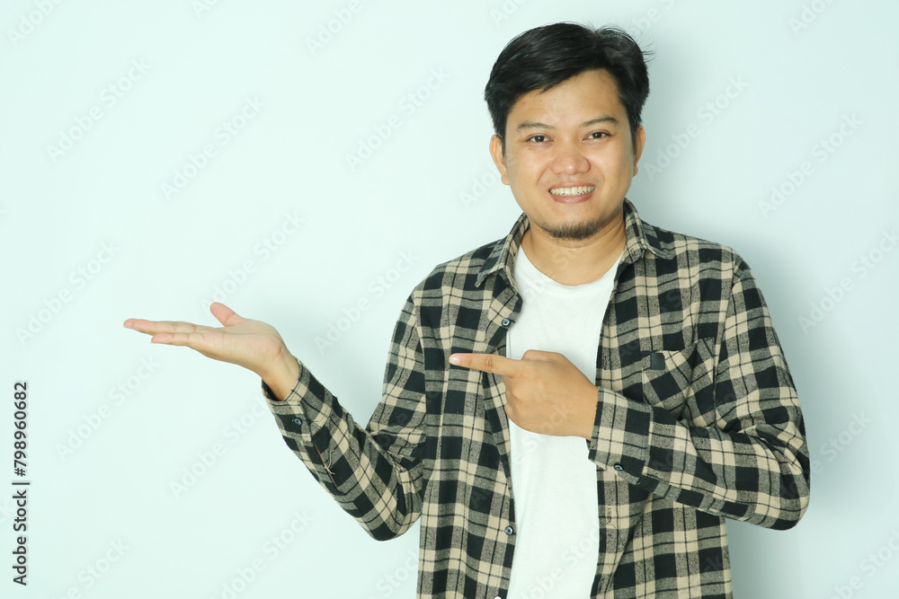 Young Asian man wearing brown flannel shirt smiling while pointing to his open right hand palm Young Asian man wearing brown flannel shirt smiling while pointing to his open right hand palm
