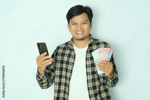 Young Asian man wearing brown flannel smiling happy at camera while holding mobile phone and money photo
