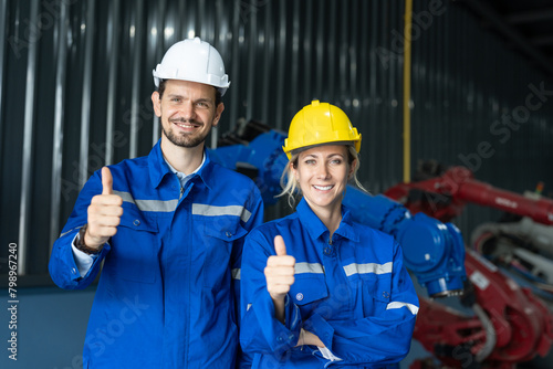 Confident male and female engineers giving thumbs up in an industrial setting with machinery in the background.