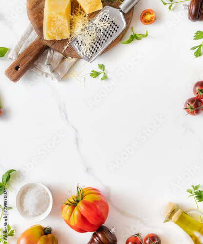 Frame of Italian food cooking ingredients background with fresh vegetables, herbs, spices olive oil and cheese on white stone table top view. Healthy eating