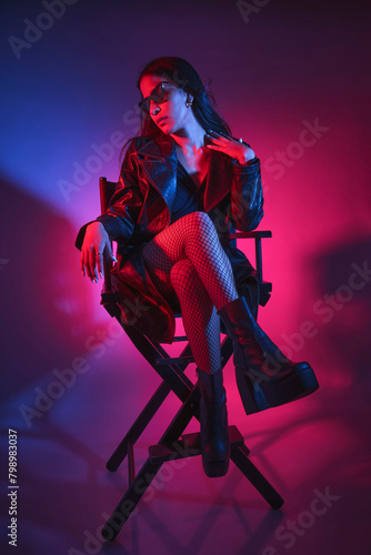 A woman is sitting on a chair in a black jacket and black stockings