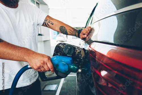 Cropped image of male holding nozzle charging vehicle car with petrol and oil on station, young man pumping benzene to automobile tank through hose on service, environment pollution concept photo
