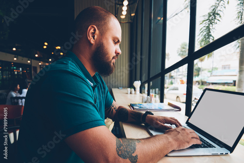 Skilled male freelancer using laptop computer with mock up screen and wifi in cafeteria for remote job, concentrated guy keyboarding on netbook  searching information online for e learning courses photo