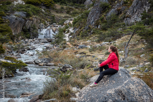 Mujer turista senatada en una roca mientras disfruta de las vistas de un bosque patagonico y sus arroyos