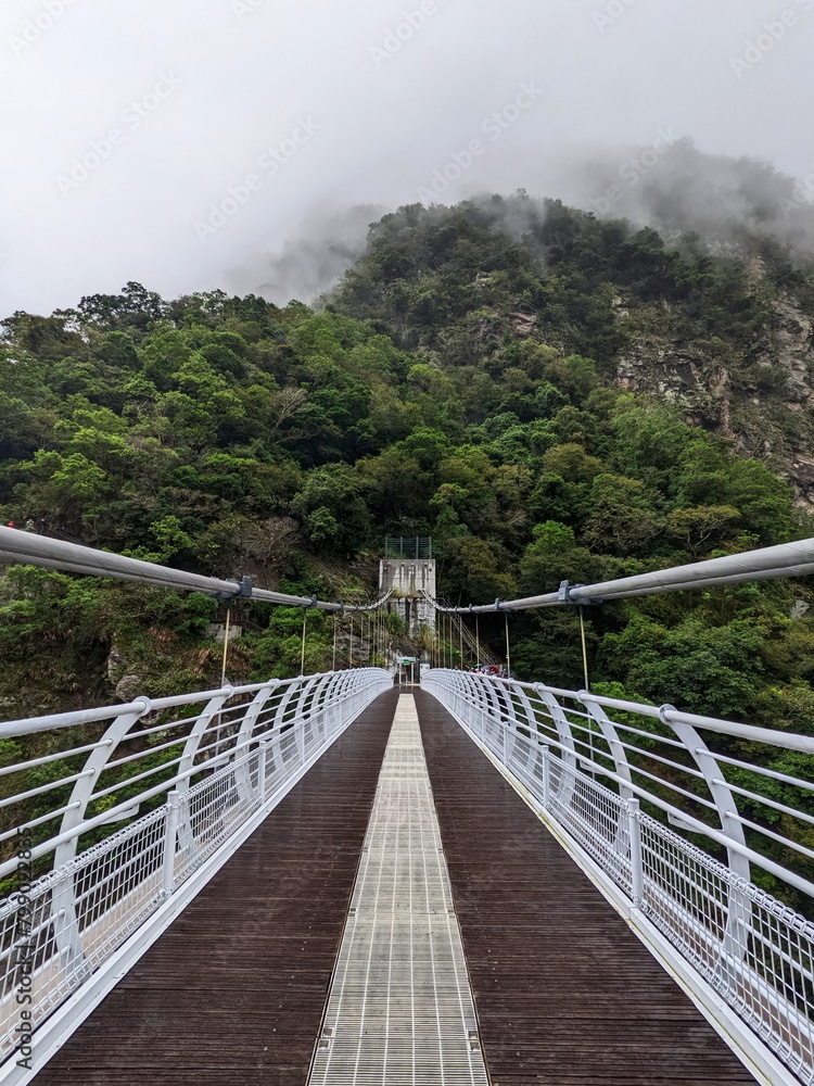 Taroko, Taiwan - 11.26.2022: Empty symmetrical Buluowan Cable Suspension Bridge over Liwu River gorge on a rainy day with mist on the mountains before the 403 earthquake during the pandemic Taroko, Taiwan - 11.26.2022: Empty symmetrical Buluowan Cable Suspension Bridge over Liwu River gorge on a rainy day with mist on the mountains before the 403 earthquake during the pandemic