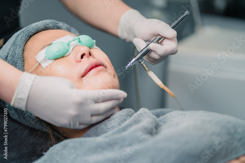 doctor laser goggles asian woman face for treatment. woman sleep wearing glasses block light got laser facial skin operation. asian patient sleep while surgery doctor doing light treatment on face