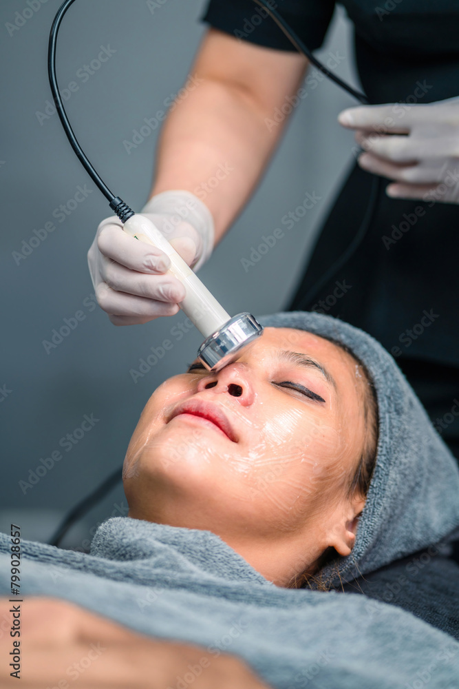 Naklejka premium therapist doing cavitation operation asian woman for wrinkles fat removal. clinic doctor using cavitation equipment to remove wrinkles on woman skin. female patient get cavitation on skin by surgeon