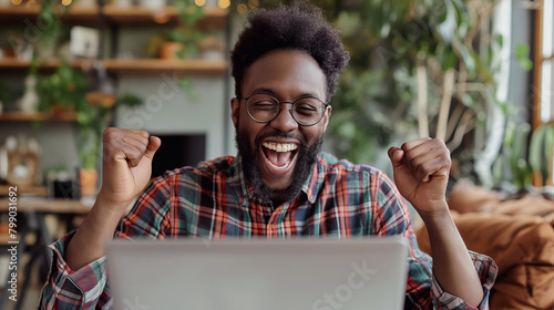 black african american male student working on laptop with hands in the air, celebrating success, happy about success, profit, good grades