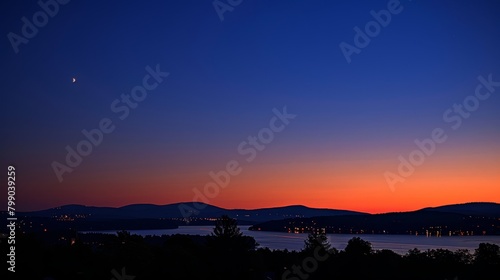   View of sunset over tranquil lake, mountains distantly silhouetted, crescent moon gracing night sky photo