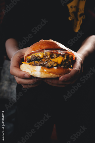 a person holding a juicy double cheeseburger hamburger dark moody
