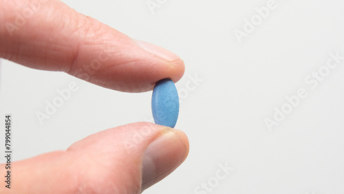 Blue pill for impotence or erectile dysfunction. Hand holding pill between finger and thumb.