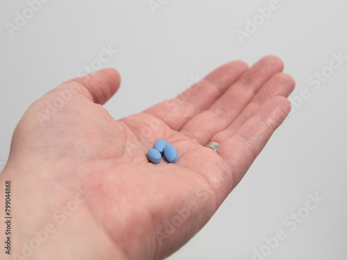 Hand holding blue pills for treating impotence or erectile dysfuntion