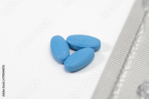 Blue pills for impotence or erectile dysfunction on a white table with foil wrapping