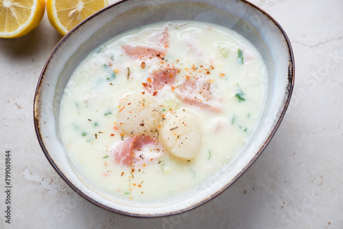 Bowl of milky chowder with scallops and bacon, horizontal shot on a light-beige stone background, elevated view